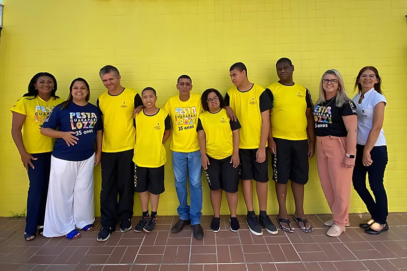 Grupo de jovens e adultos atendidos pela assistência social junto à equipe na fachada da Pestalozzi Guarapari.